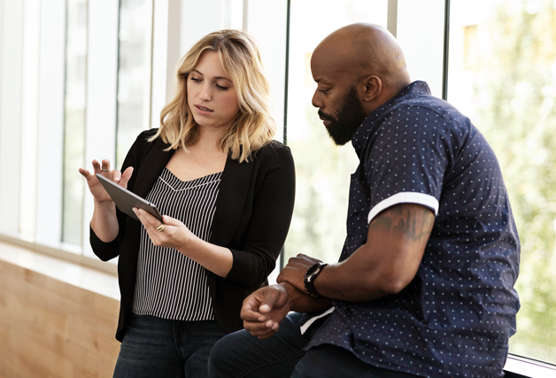 A man and woman looking at a tablet computer in the hallway of an office