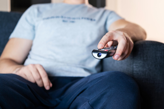 Photo of a person sitting on a couch pointing television remote