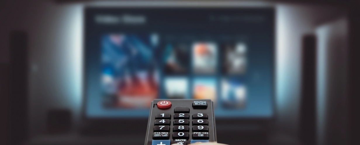 Person using a remote control to navigate video-on-demand (VOD) services on a large television screen displaying various streaming options.