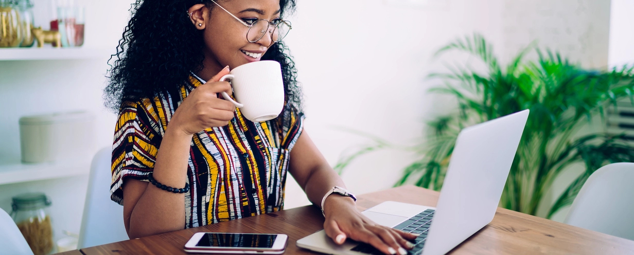 Photo of a person looking at their laptop while holding a white mug