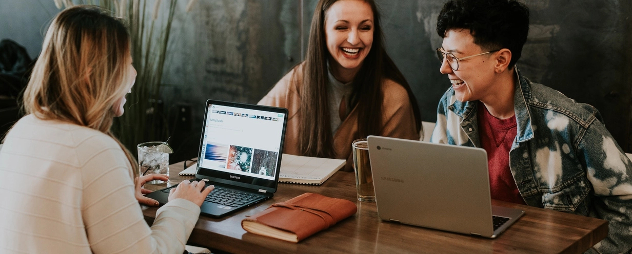 Photo of 3 people sitting at a table in a coffee shop with their laptops open