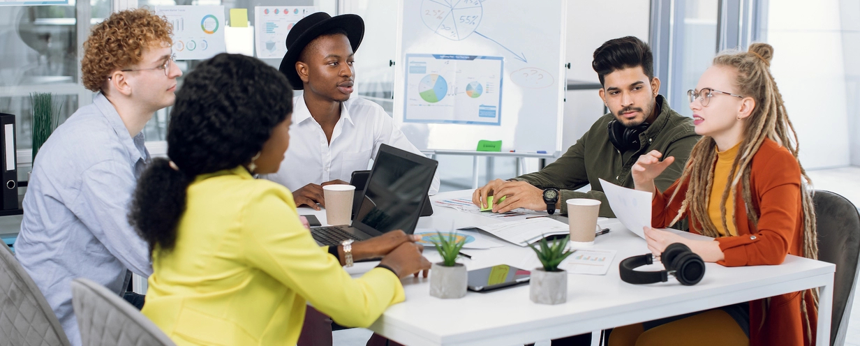 5 young professionals sitting at a table in an open office