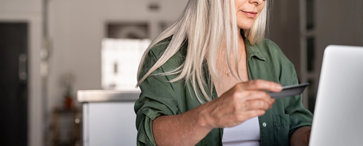 Photo of a person looking at their credit card while typing on their laptop