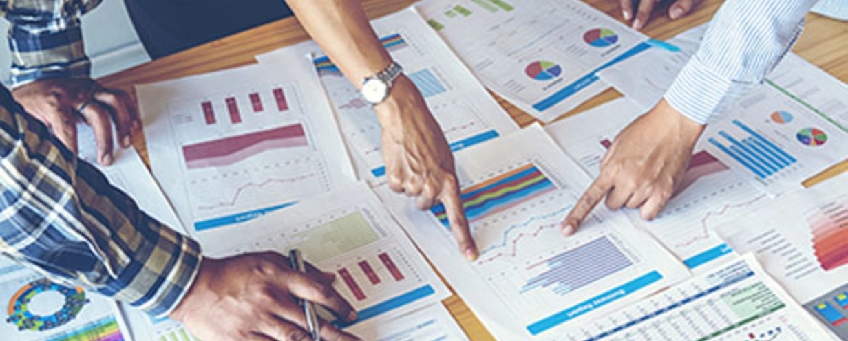 Team of 3 people pointing to charts and graphs on sheets of paper on a conference table