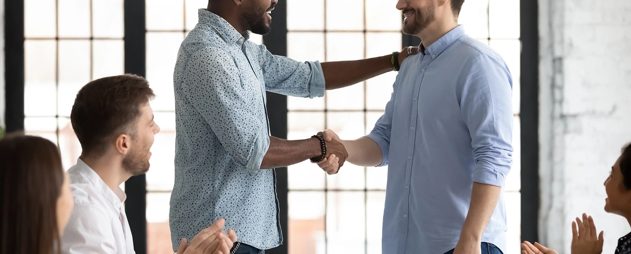 Photo of two people shaking hands with team members around a conference table clapping