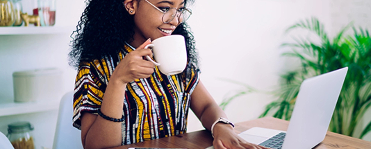 Woman sitting at desk with laptop and phone holding a coffee mug