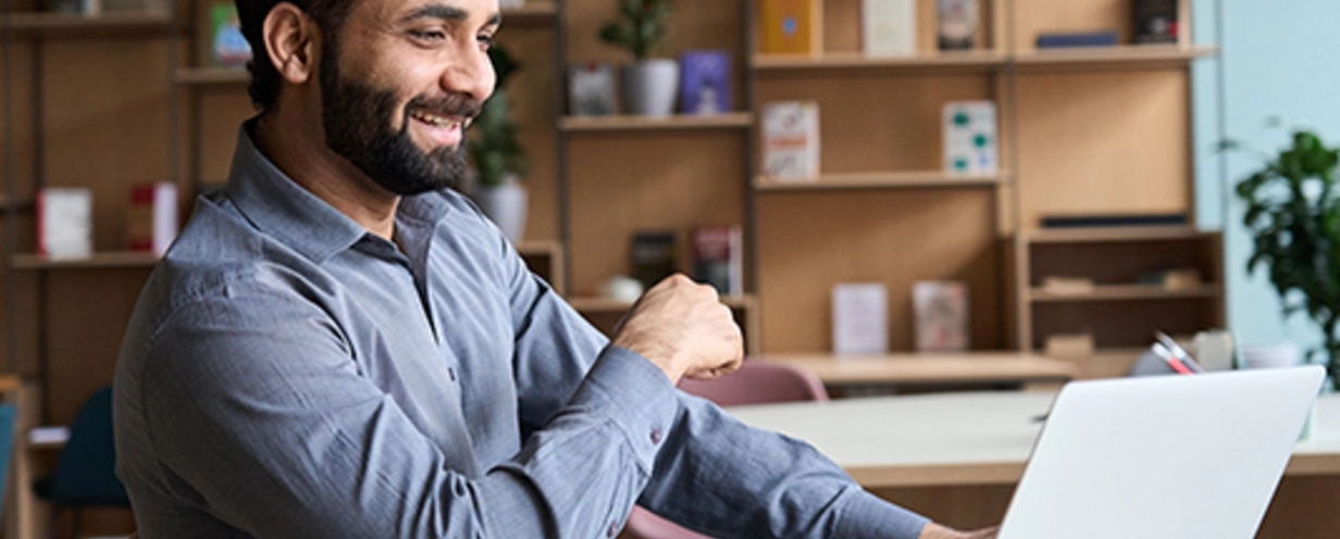 Man smiling sitting in office desk looking at laptop