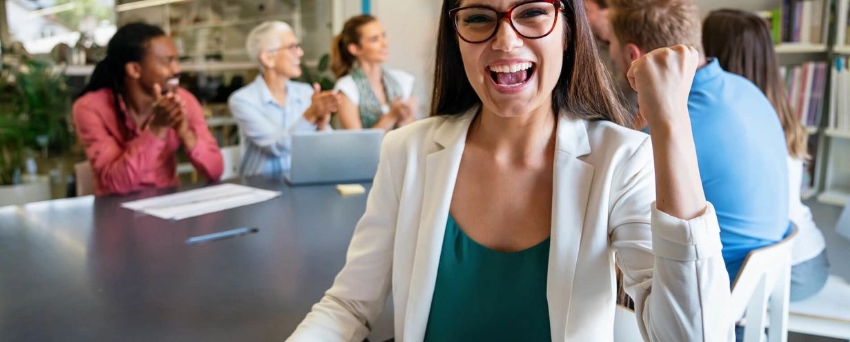 Smiling woman celebrating with raised fist with smiling colleagues in the background