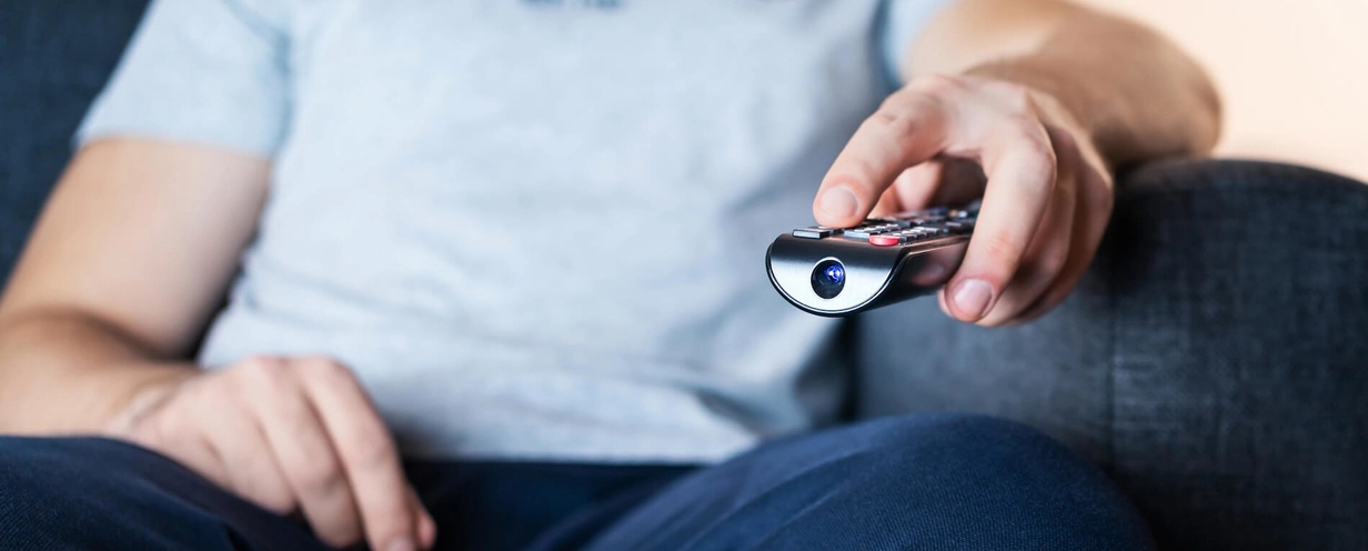 Photo of a person sitting on a couch pointing television remote 