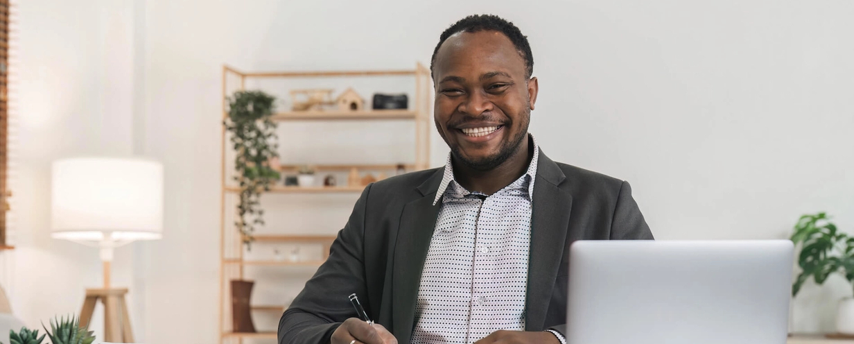 Smiling man sitting at a desk with papers and a laptop