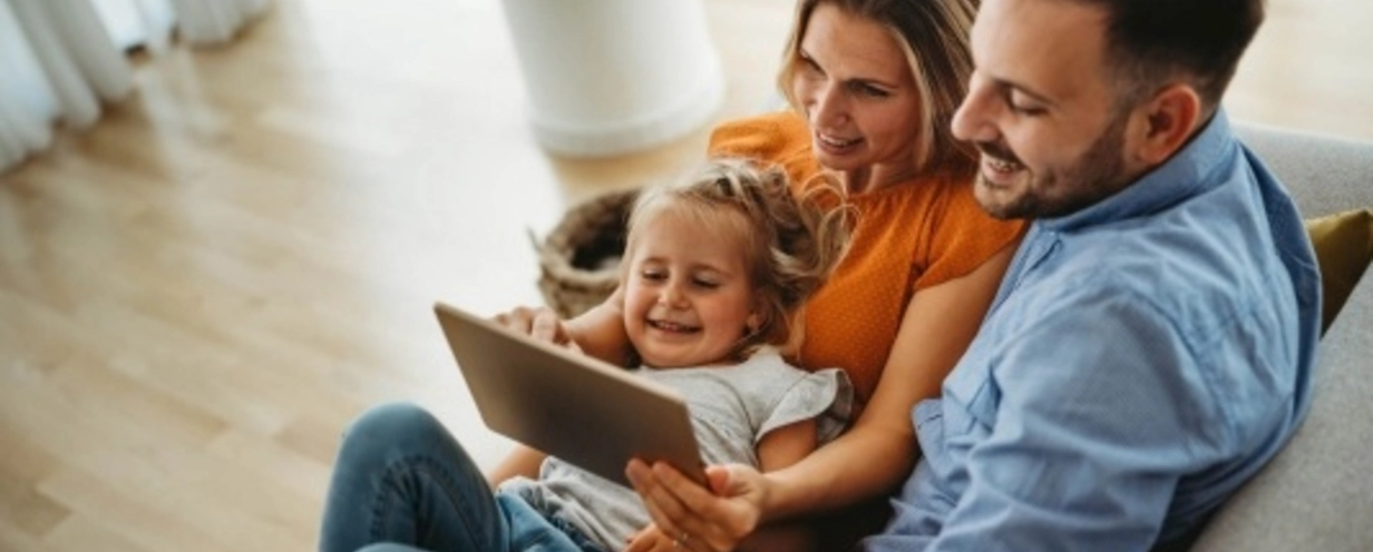 Family of three sitting together while looking at a tablet