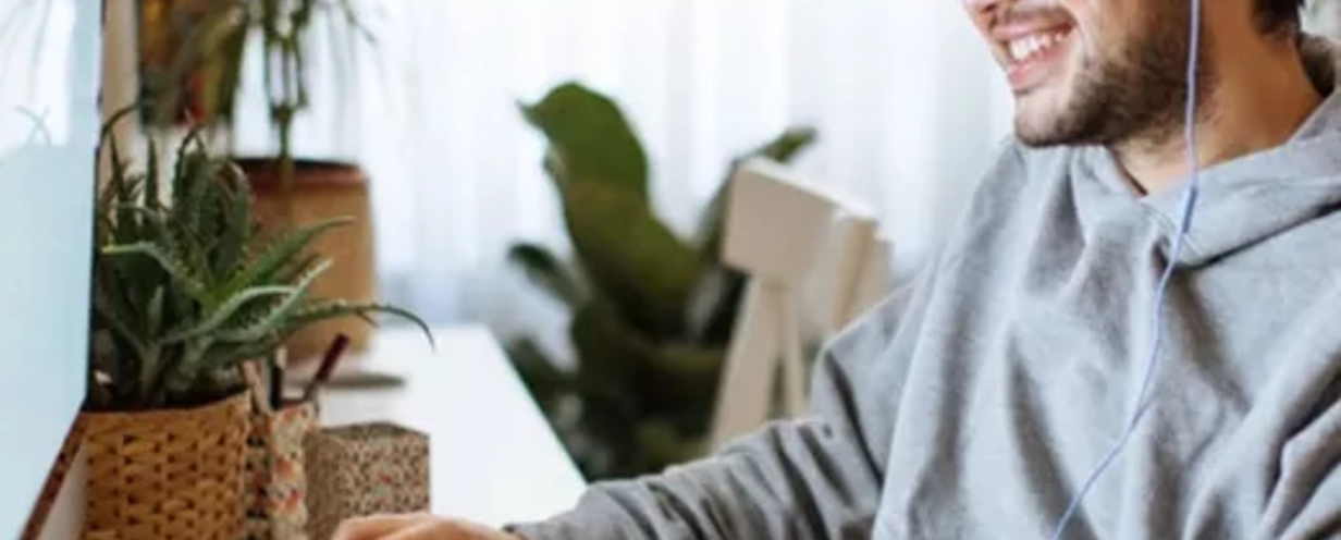 Man sitting at his desk with headphones on, smiling at his computer monitor