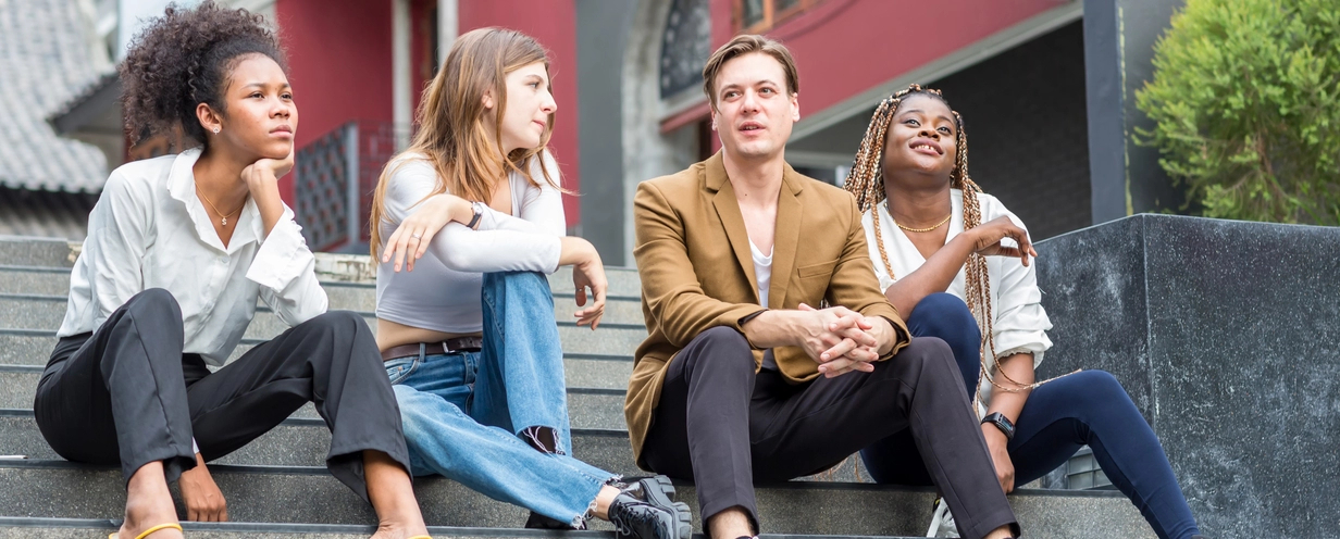 Group of young adults sitting on steps outside in front of a building