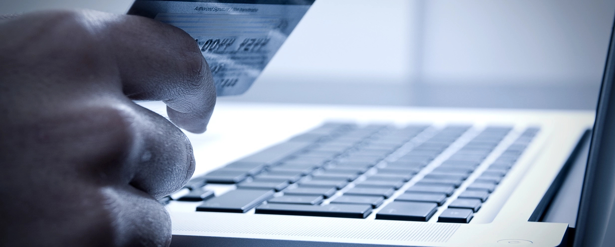 Photo of a laptop with a hand holding a credit card illustrating digital checkout