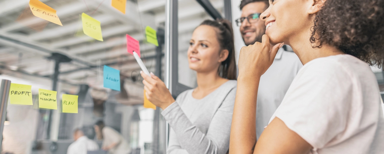 Photo of 3 people at a glass wall using post-it notes to map out the customer journey