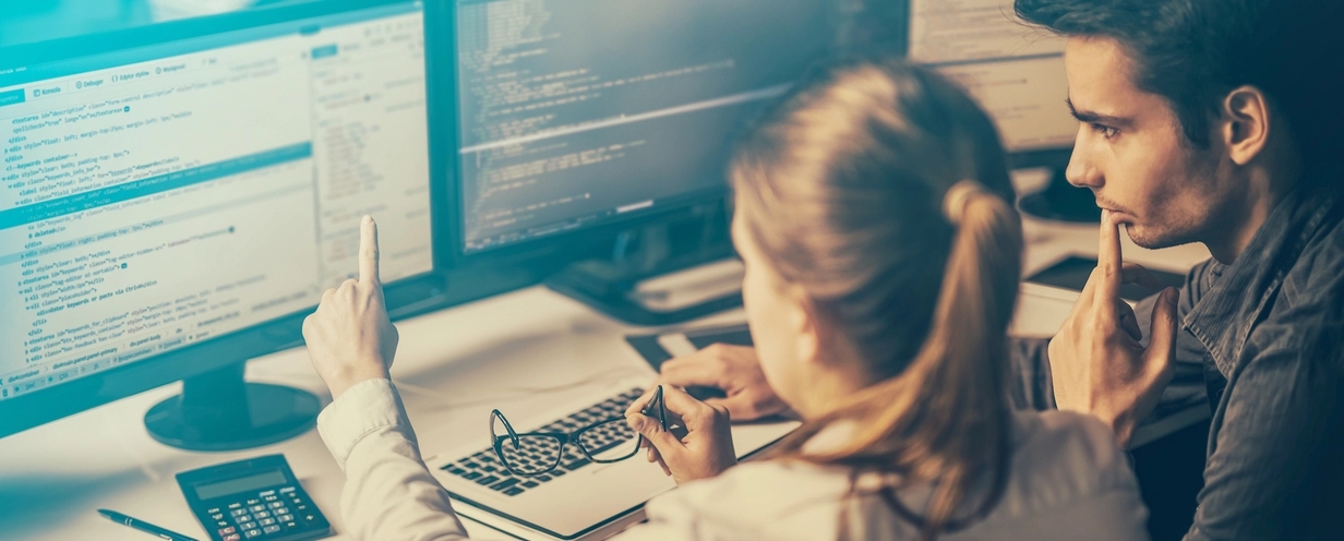 Photo of two professionals sitting in front of multiple computer monitors