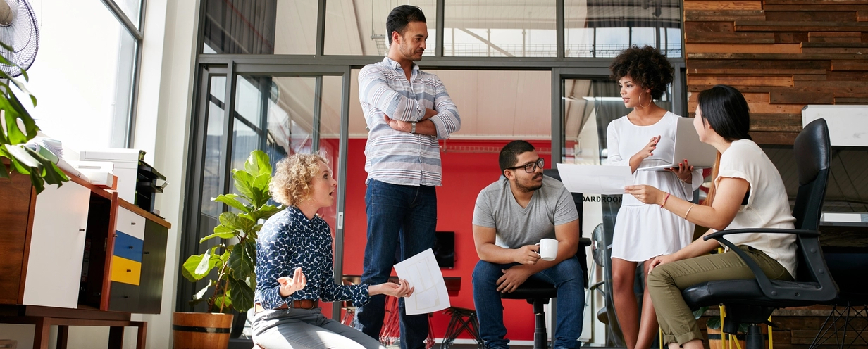 Team sitting in a circle and listening to talking woman holding her laptop