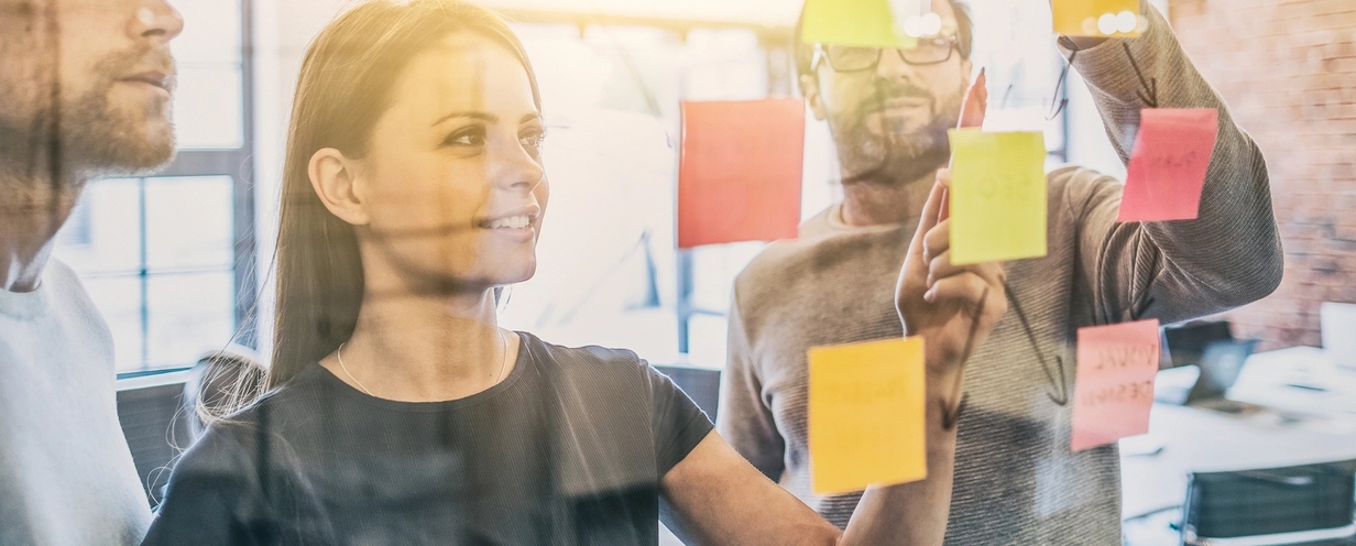 Photo of 3 business people reviewing sticky notes on a window wall