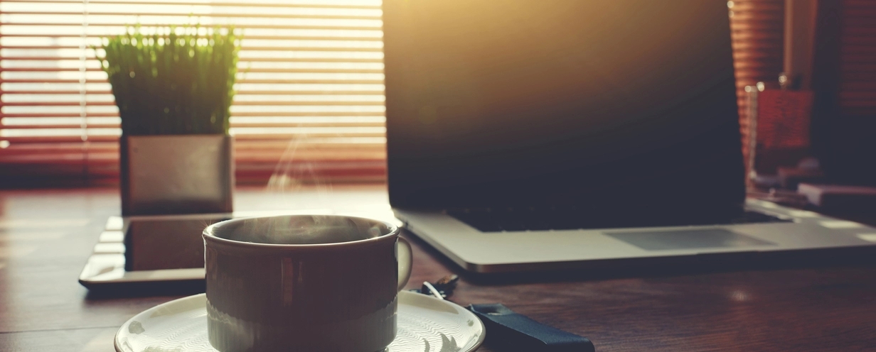 Photo of a laptop on a desk with a cup of hot coffee