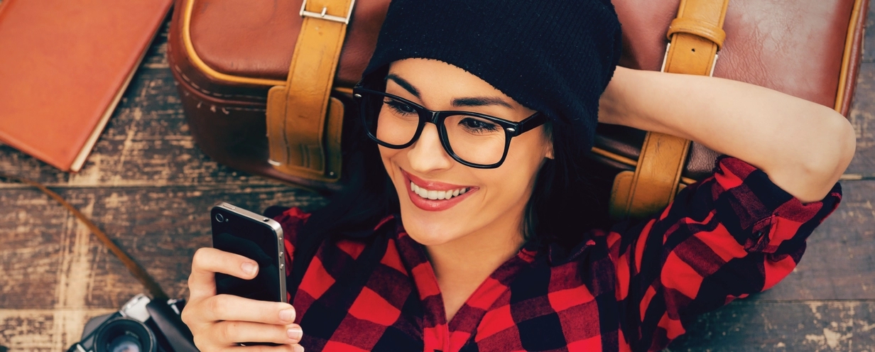 Millennial woman resting head on suitcase while looking at mobile phone