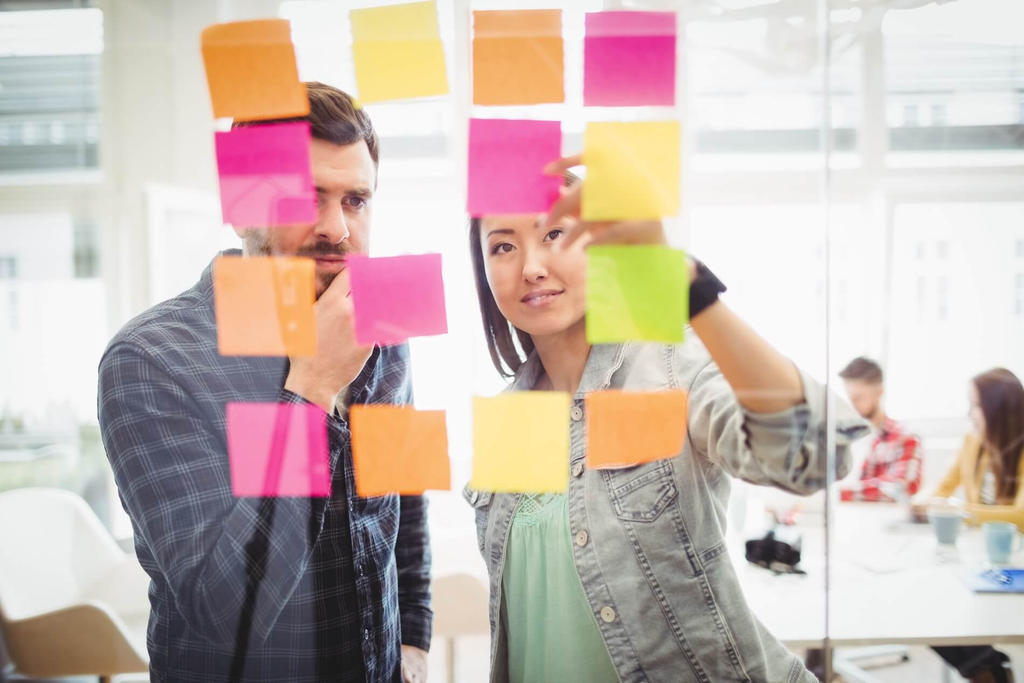 Two designers reviewing sticky notes on a glass board.