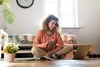 Photo of a woman sitting on the floor of a well lit room holding her credit card while looking at her laptop