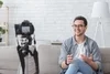 Smiling man sitting in front of a camera on a tripod