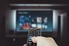 Person using a remote control to navigate video-on-demand (VOD) services on a large television screen displaying various streaming options.