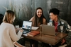 Photo of 3 people sitting at a table in a coffee shop with their laptops open