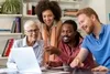 4 people in an office setting gathered around a laptop