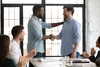 Photo of two people shaking hands with team members around a conference table clapping