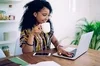 Woman sitting at desk with laptop and phone holding a coffee mug