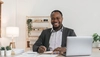 Smiling man sitting at a desk with papers and a laptop