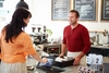 Photo of someone checking out at a coffeeshop using a laptop as a barista smiles