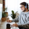 Man sitting at his desk with headphones on, smiling at his computer monitor