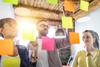 3 people developing a plan with colorful sticky notes on a clear board.