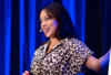 Female speaker with blue background and smiling at the crowd