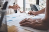 Photo closeup of two pairs of arms reviewing a printed presentation on an office desk