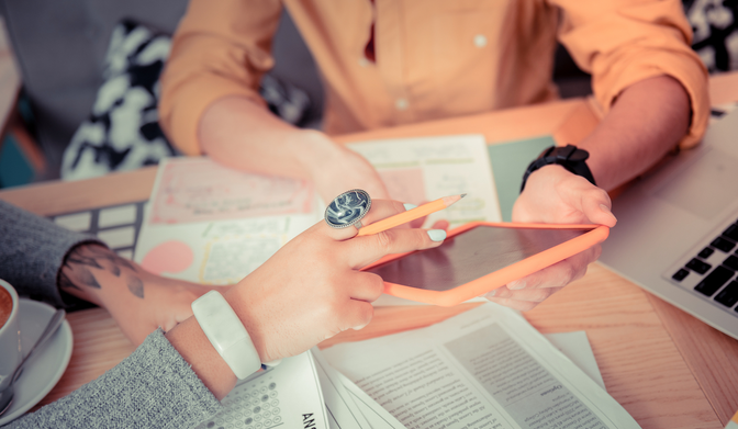Photo of 2 people looking at a tablet at a conference table