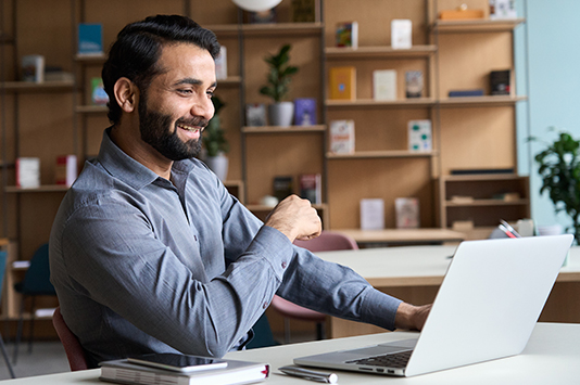 Man smiling sitting in office desk looking at laptop