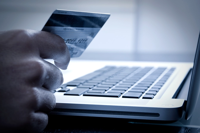 Photo of a laptop with a hand holding a credit card illustrating digital checkout