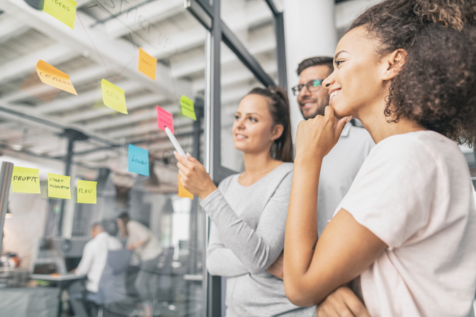 Photo of 3 people at a glass wall using post-it notes to map out the customer journey