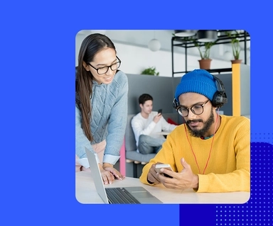 Photo of man and woman in office chatting at a desk looking at mobile phone